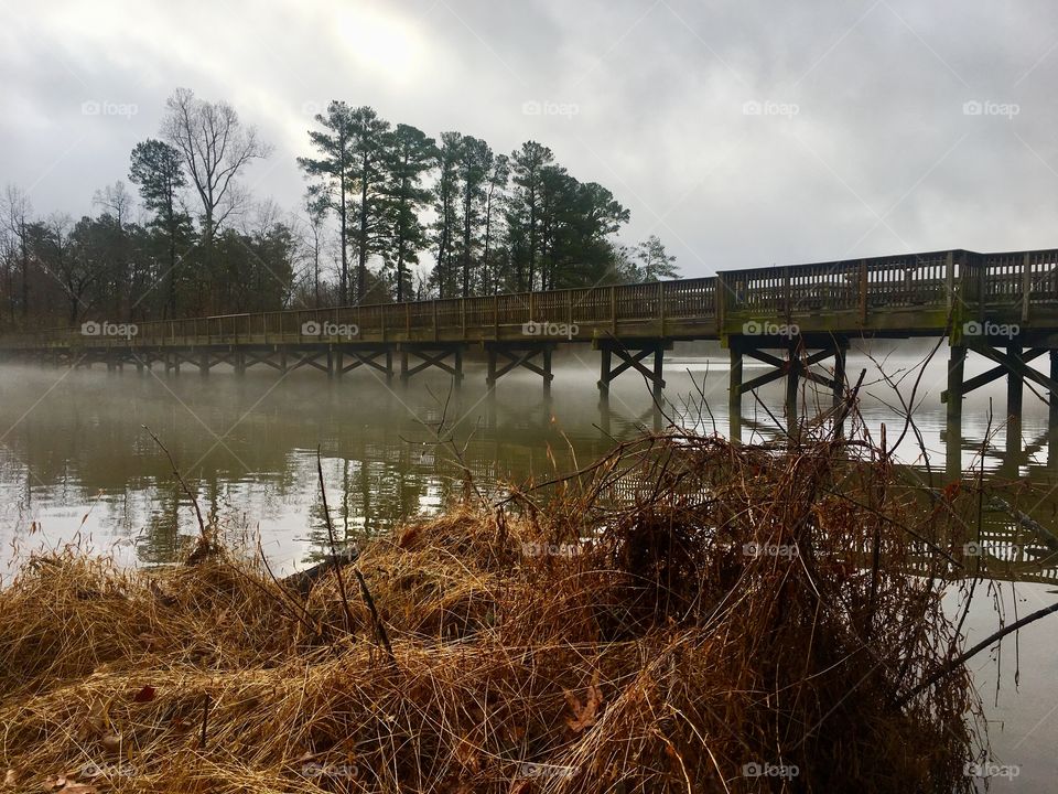 A gentle fog creeps beneath the wooden bridge in the early morning 