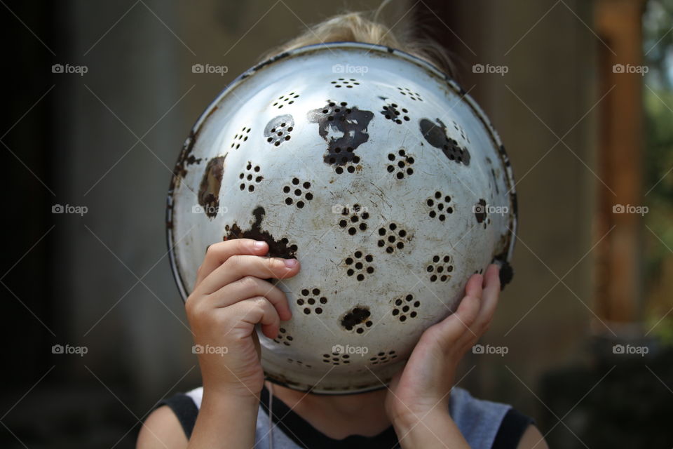 boy covering his face with an old colander