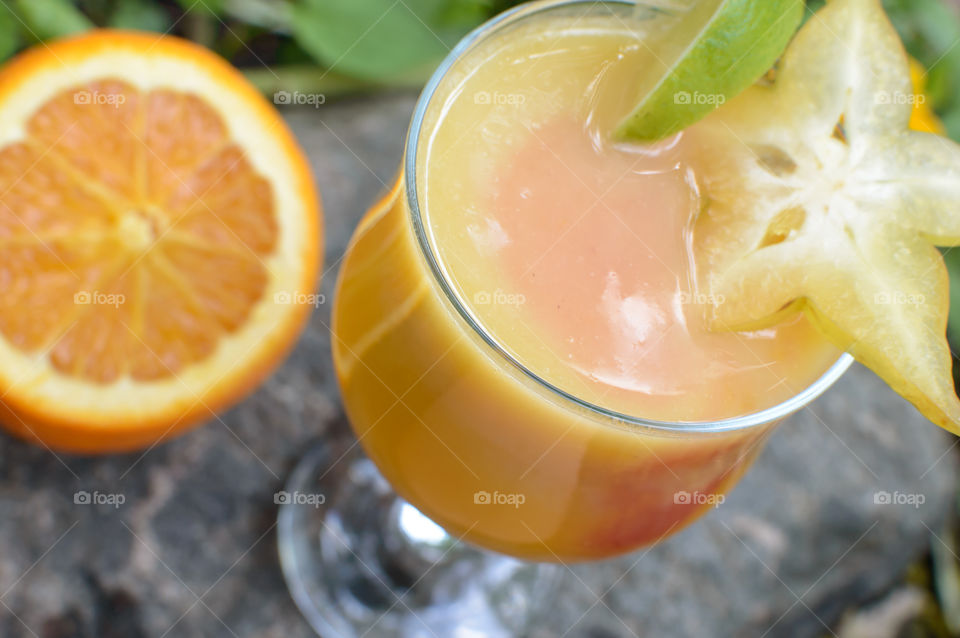 High angle view of multi colored fresh fruit smoothie creamy orange with pink center on stone background with sliced orange, lime and star fruit ingredients fresh food photography 