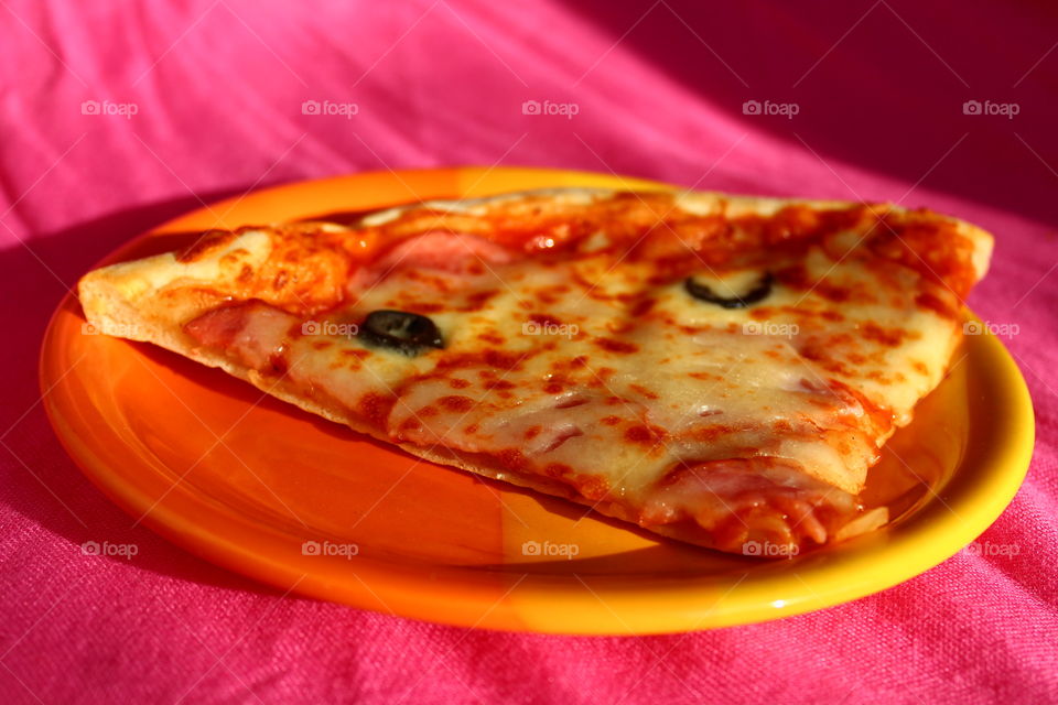 Slice of pizza in a orange plate on a pink background