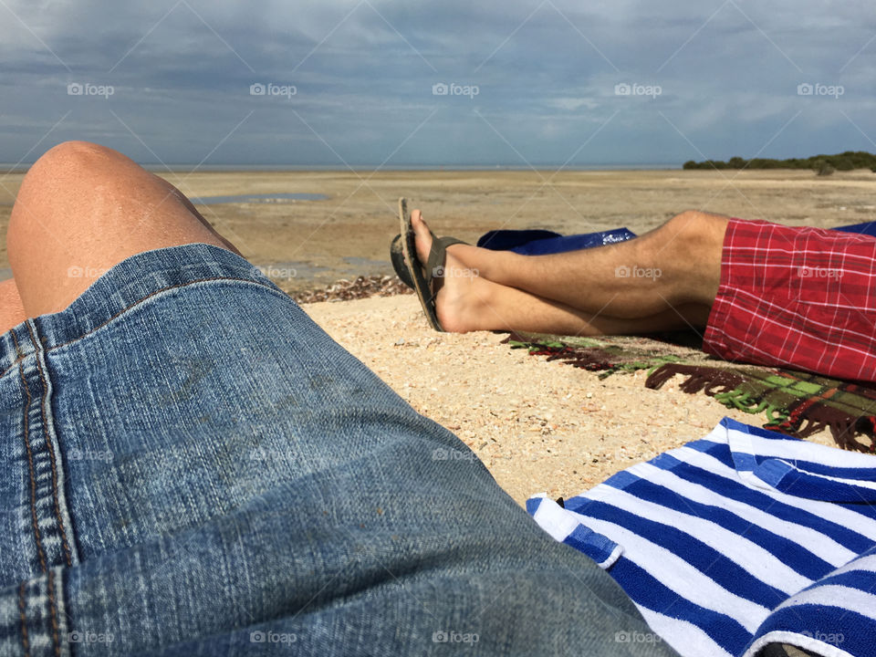 Leg view man and woman laying out on secluded beach, toward horizon, towels, legs, tanned, tropical, outdoors 