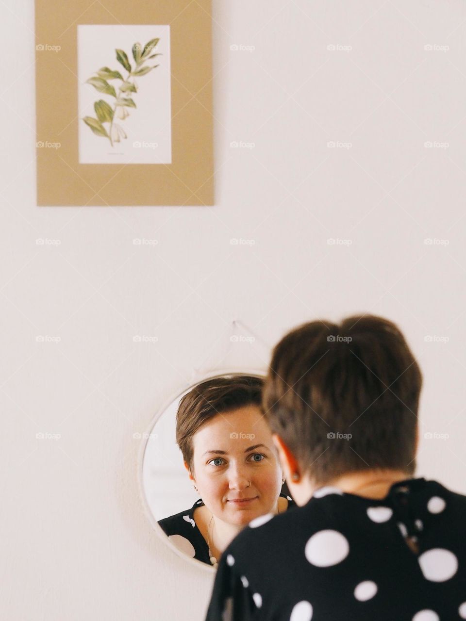 Young beautiful woman with short dark hair looking at mirror 