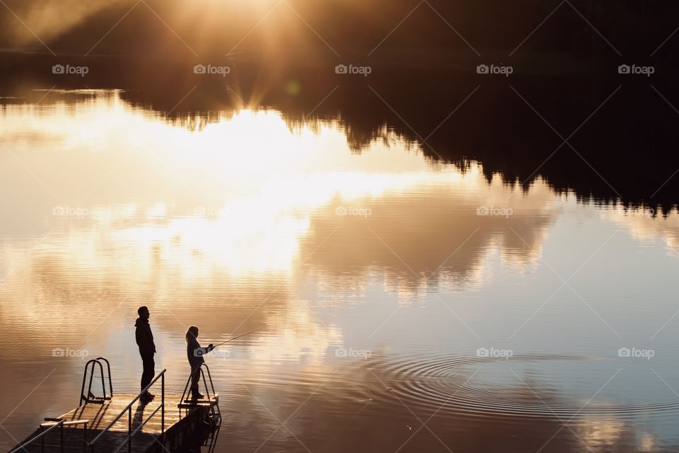 Silhouette of people fishing on a wooden pier at sun set