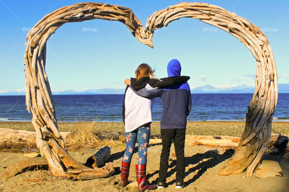 What’s that driftwood heart doing on the beach?? Two young friends pose under the heart on our local beach.  A favourite spot for wedding photos! 