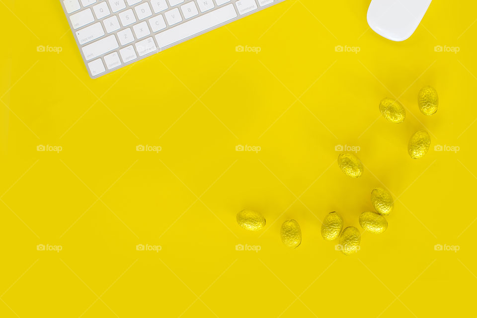 Yellow Easter desktop with keyboard and mouse and yellow foil chocolate Easter eggs; flat lay with copy space 