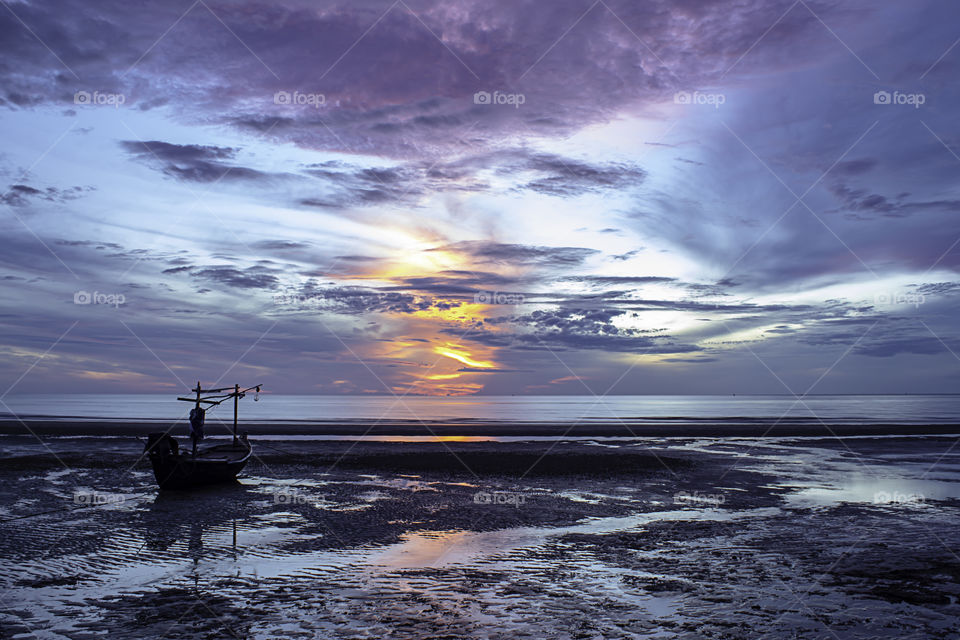 The morning sun light in the sea and the boat on the beach.