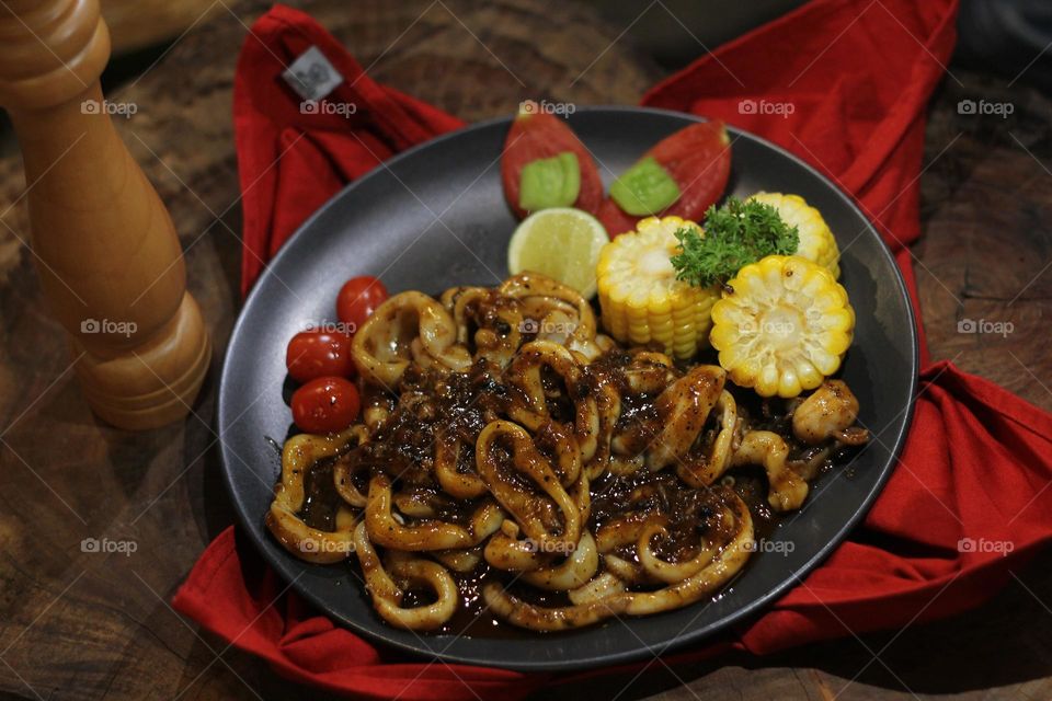 Close-up portrait of squid rings seasoned with barbecue sauce served on a black plate on a wooden table, wooden barbecue spice shaker background — Stock Photo