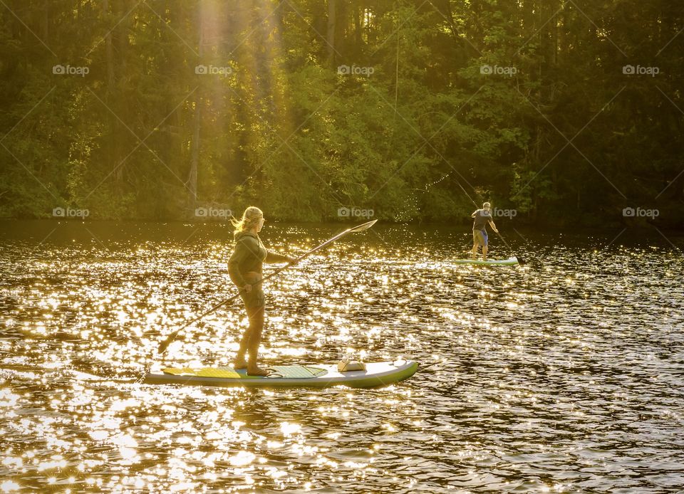 Two people paddle boarding under yellow sun beams in the evening light 