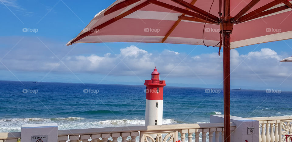 Iconic red and white lighthouse at Umhlanga Beach, taken from under a red and white umbrella with the Indian Ocean in the background