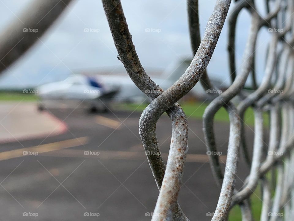 Small Airport for leisure and activities and other uses and purposes for outdoor fun and skydiving. Seeing a plane by the plane track behind a link chain fence.