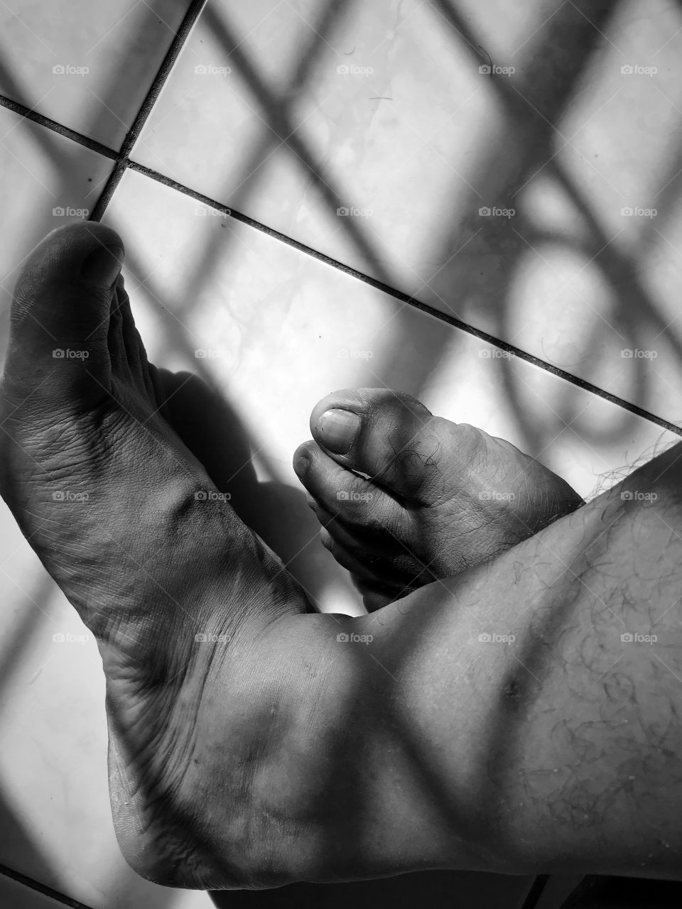 Middle age man feet in black and white, shot during perfect sunset light inside the room with the shadow of an iron window’s fence