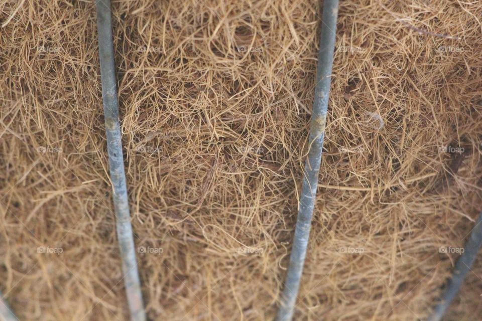 Matted stringy bits of plastic, weaved together into a basket like shape for flowers and plants