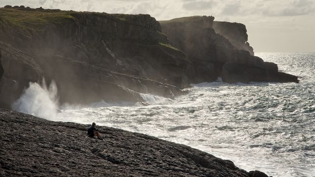 A couple of hikers rest and contemplate the sea as the waves splash next to them