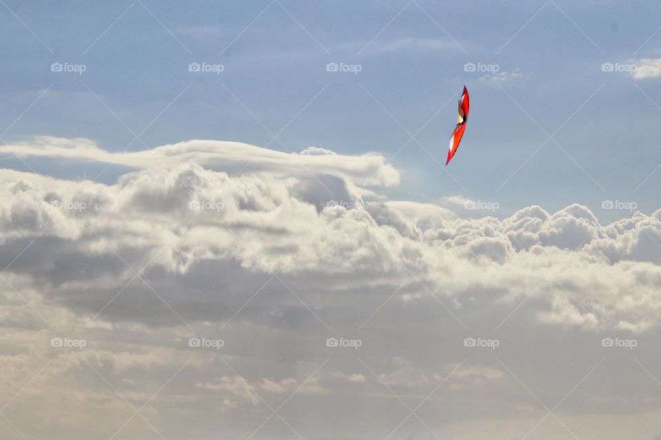 An orange kite toy flies in the blue sky with white clouds