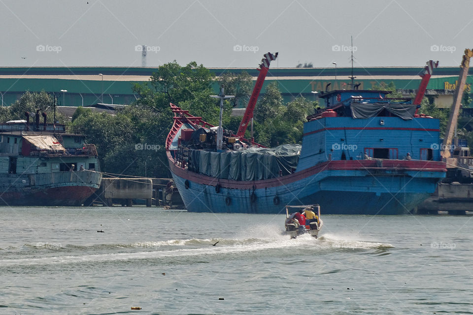 Two men in a small boat seemingly challenging a huge blue cargo barge. Port Klang, Malaysia, June 2018