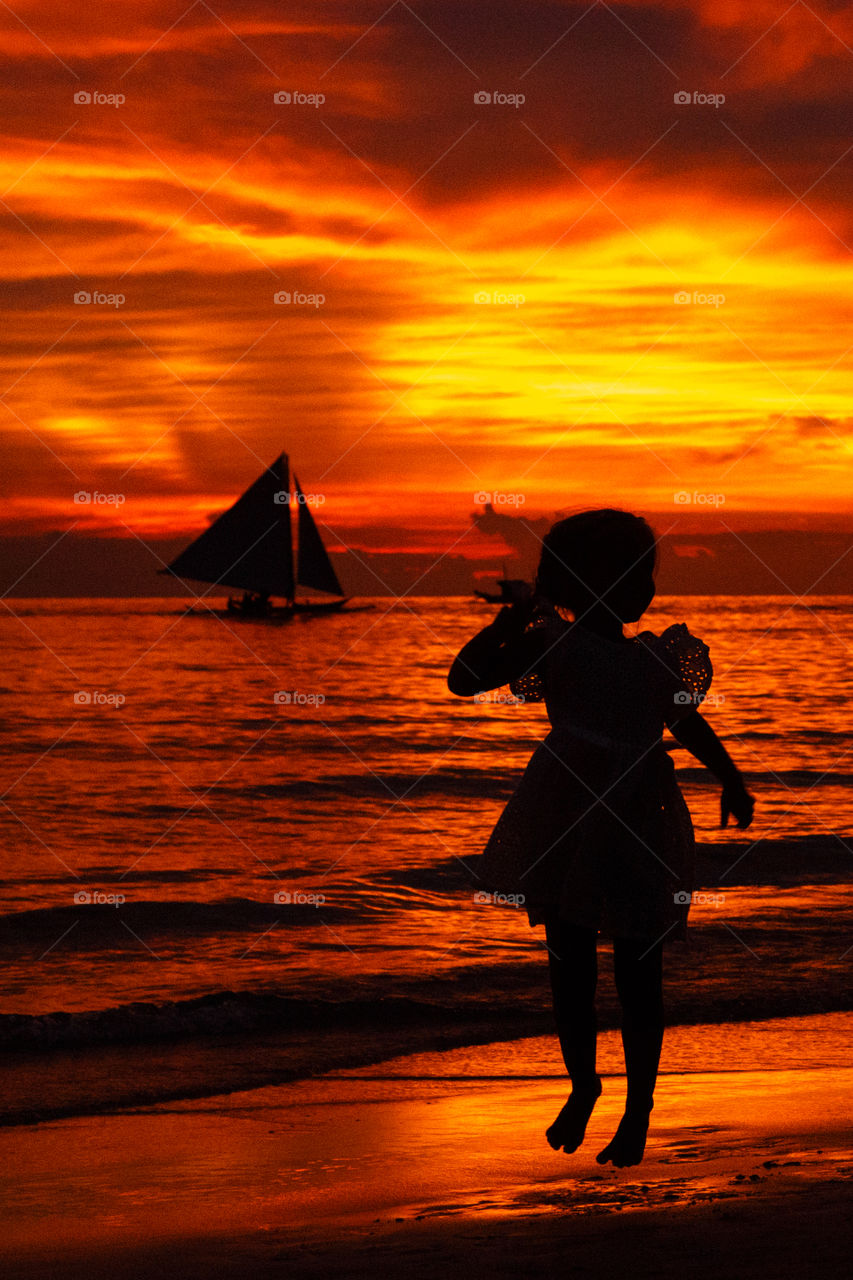 Little kid jumping on seashore on sunset 