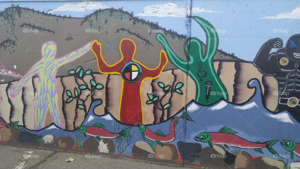 Colourful parking lot wall mural depicting local scene of river with sockeye salmon run, the surrounding hills and sky and stylized people with symbols on them.