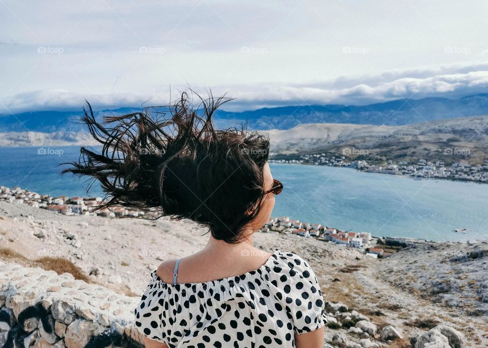 Back view of woman in a polka dots flowy dress and sunglasses with hair blown up by the wind