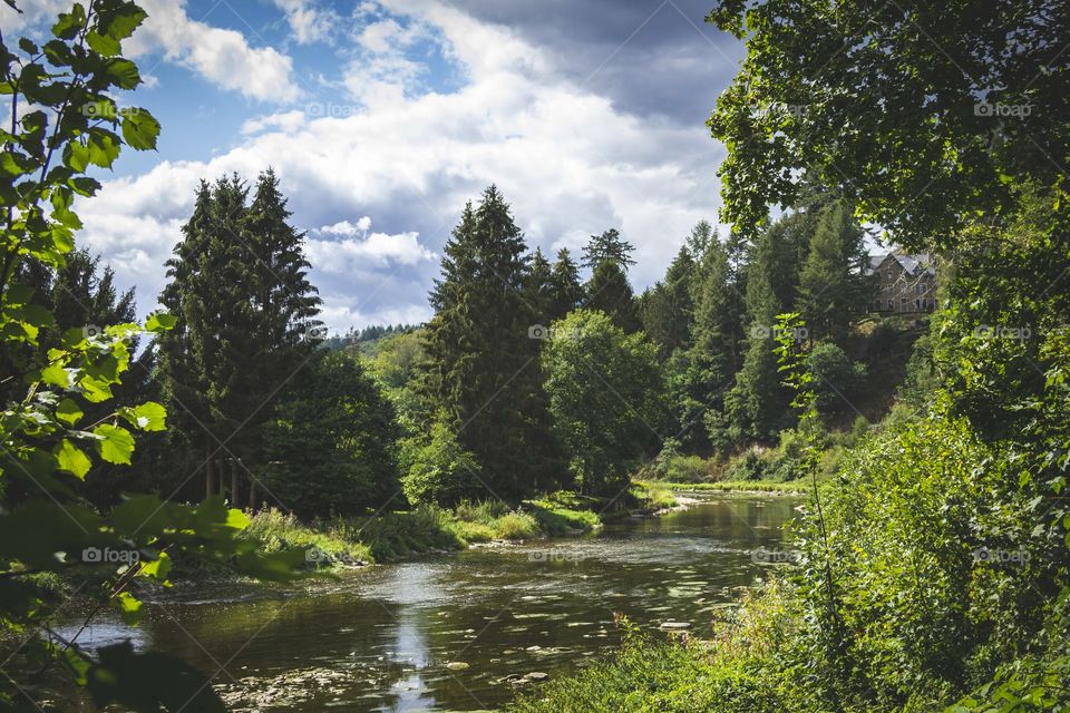 A landscape portrait of the semois in belgium. a cloudy blue sky is over the river surrounded with trees and mountains in the belgian ardennes.