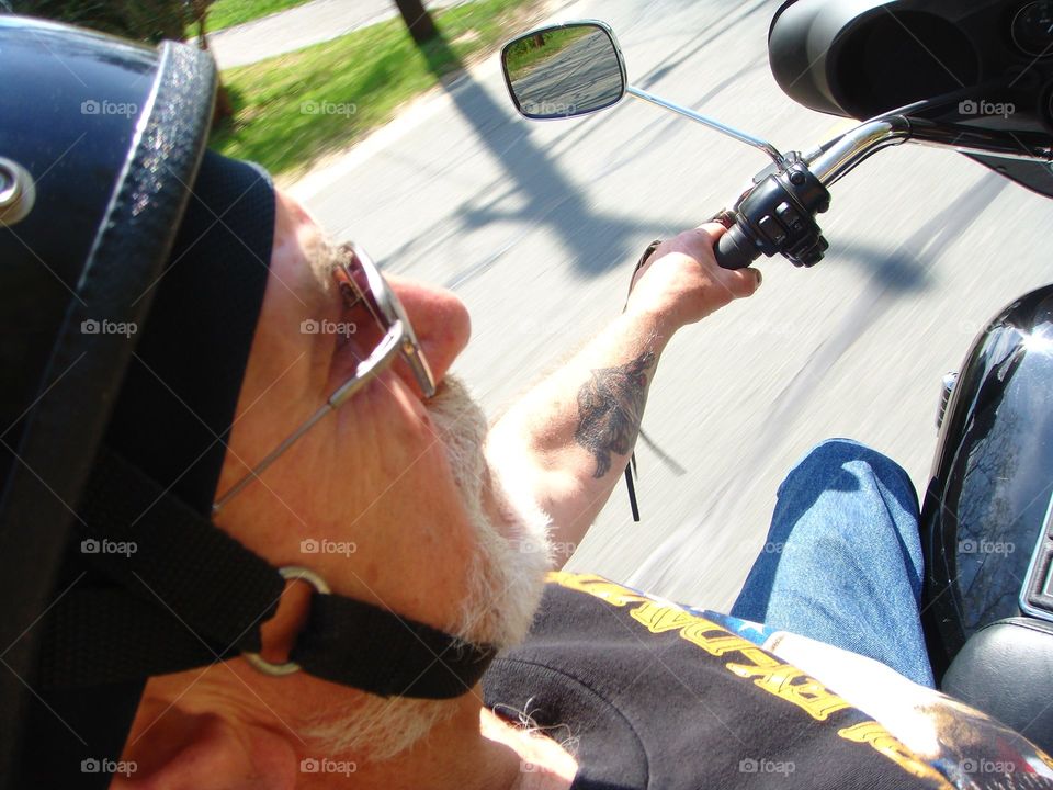 Man wearing helmet & sunglasses, driving motorcycle, pic in profile.