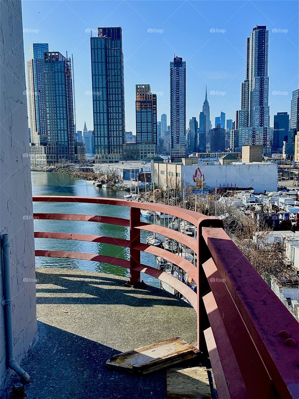 This is “Newtown Creek” seen from the central outpost of the “Pulaski Bridge” that connects “Greenpoint”, Bklyn to LIC. Straight ahead in the distance you see “Manhattan” incl. landmarks such as the “Empire State Bldg”. 2024. Hypnotic Productions