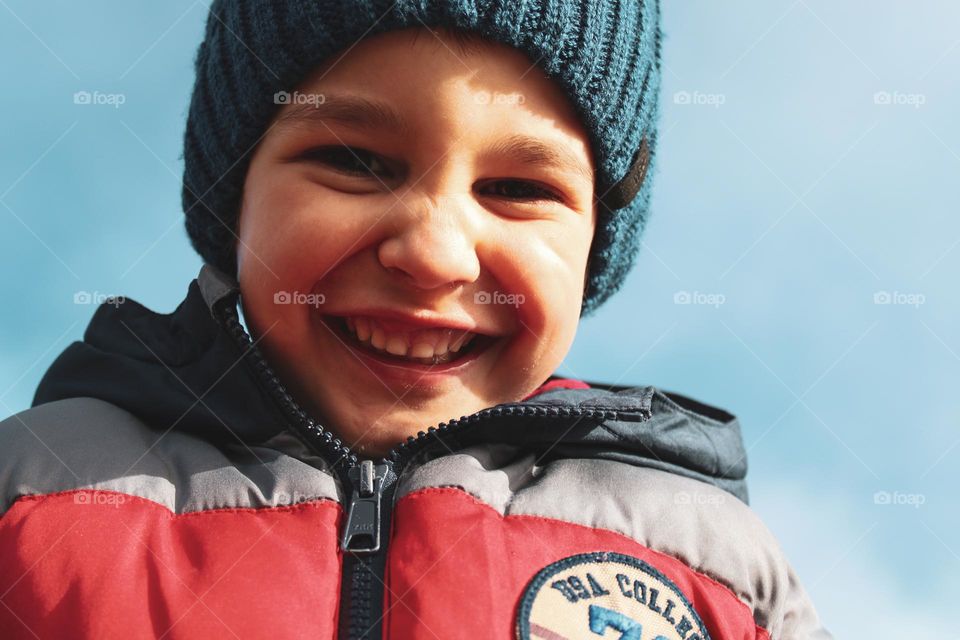 Little boy with a bonnet smiling. Blue sky background.