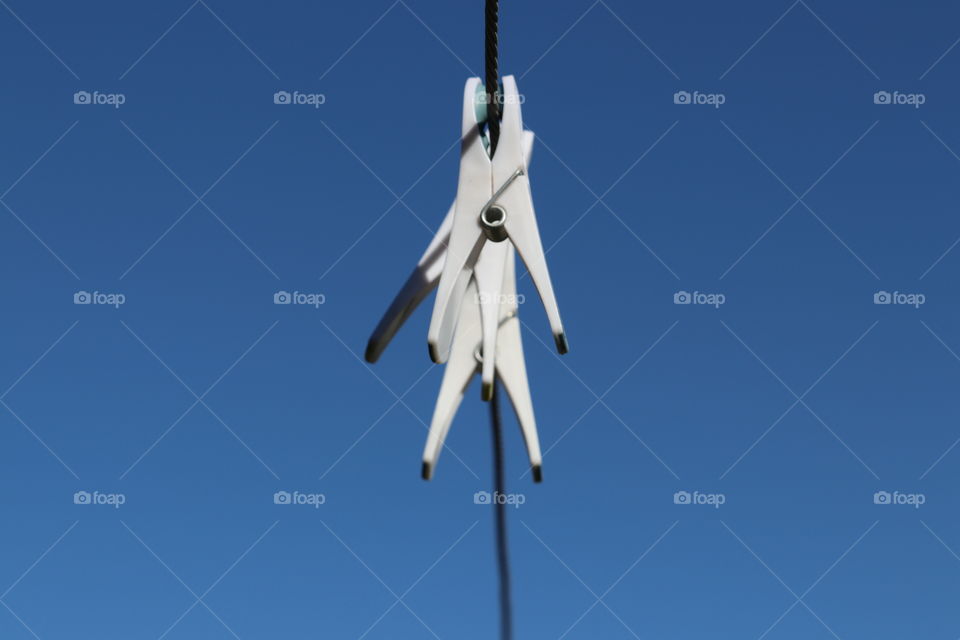 White plastic clothespins clothes pegs on wire laundry line, blue sky negative space minimalist image 