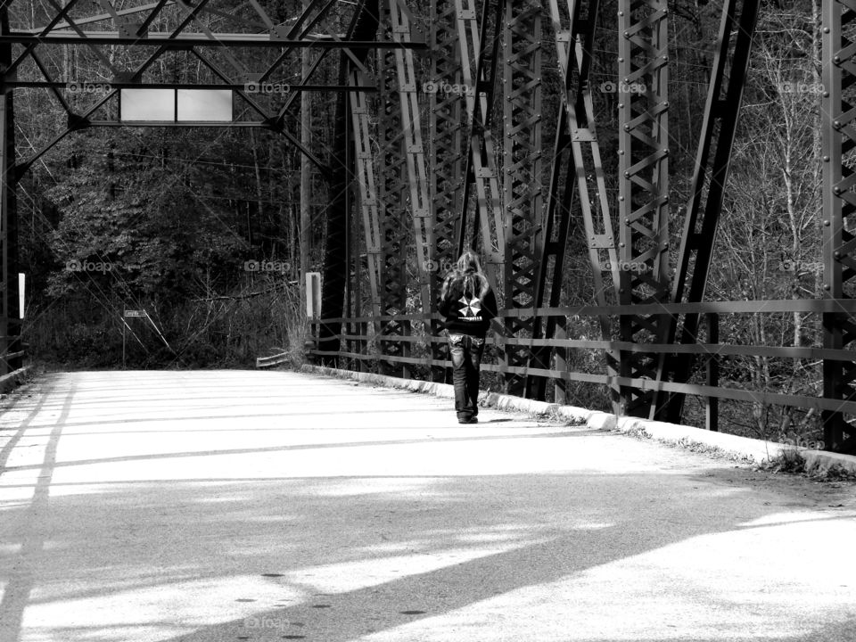 black and white photo of girl walking alone on old bridge
