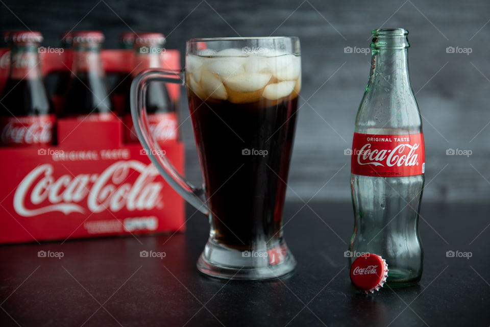 Glass filled with Coca-cola on ice with an empty glass bottle and a six-pack