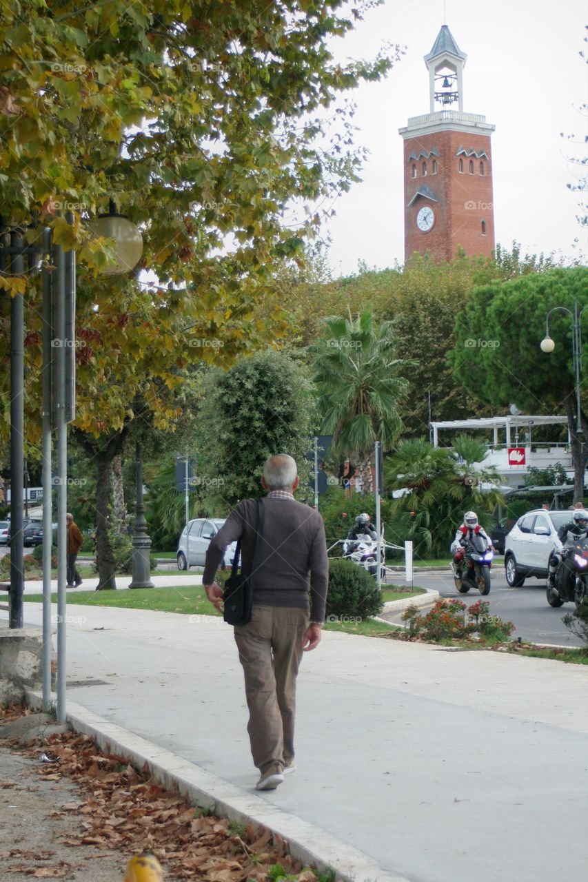 Old man looking at motorcycles passing while walking, Autumn.