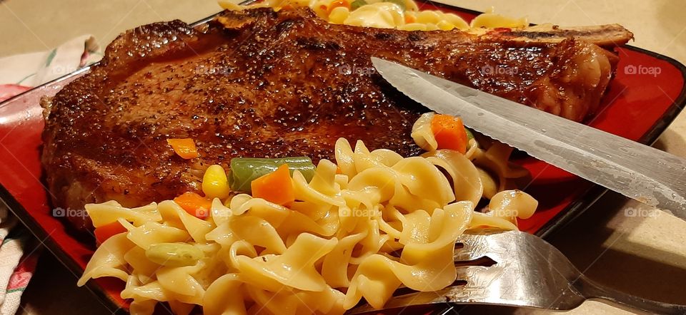 ribeye steak medium rare with buttered noodles and mixed vegetables of peas carrots green beans.