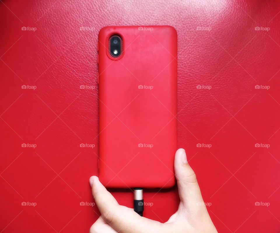 a hand holding a smartphone with a red case and charging