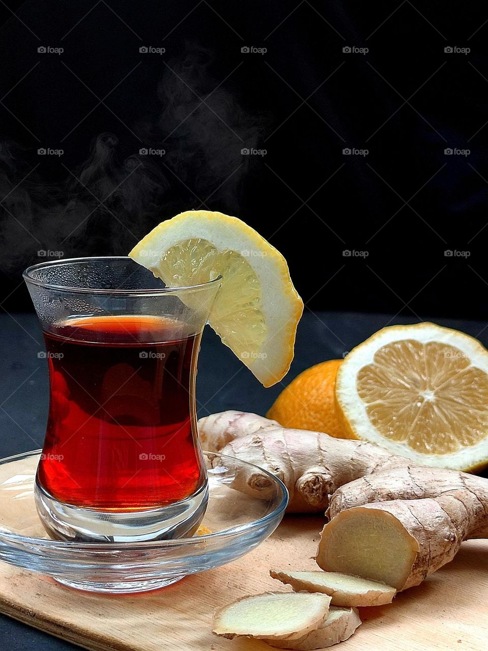 horizontal surface. Tea in an armuda glass, ginger pieces, ginger root, cut lemon. Eastern tea. Steam is visible above the glass of tea.