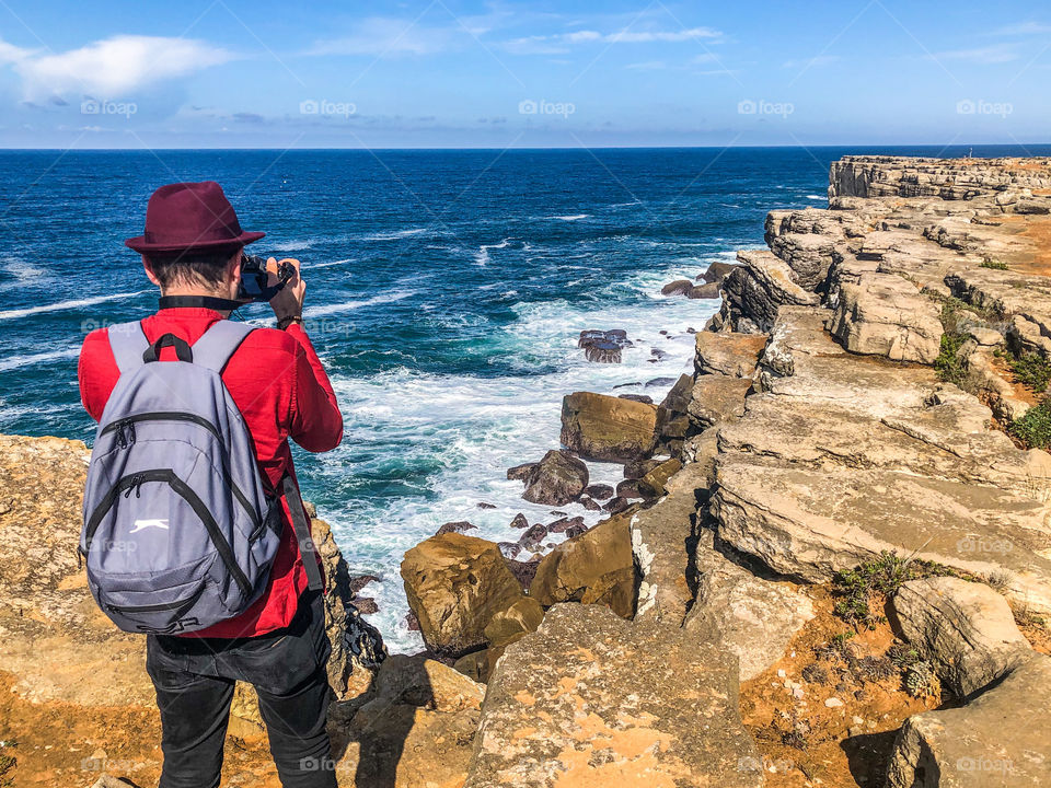 A tourist with a backpack stands by the cliff edge, taking pictures of the Atlantic Ocean