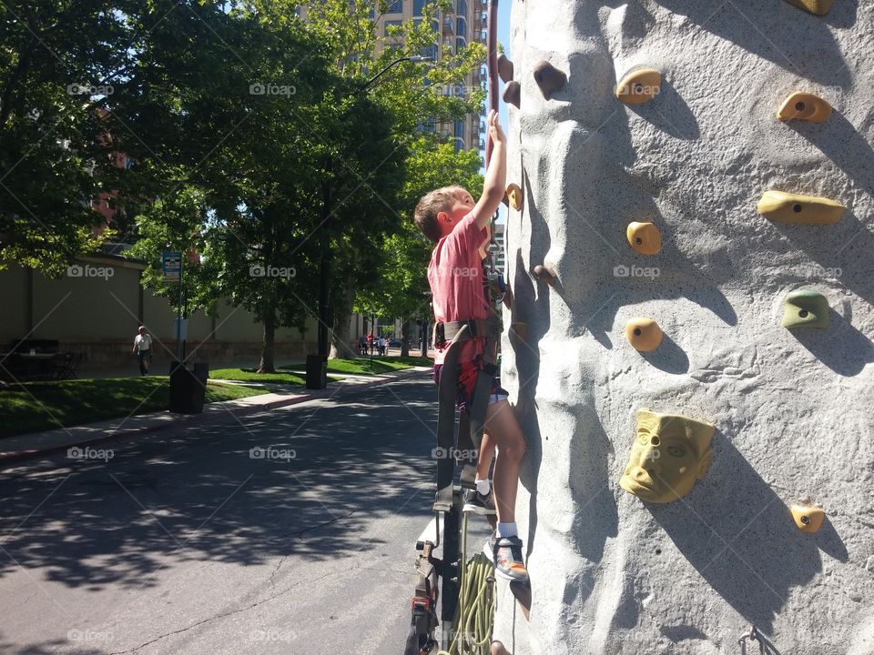 A young boy climbing a rock climbing wall at a carnival or festival in the streets of Salt Lake City.
