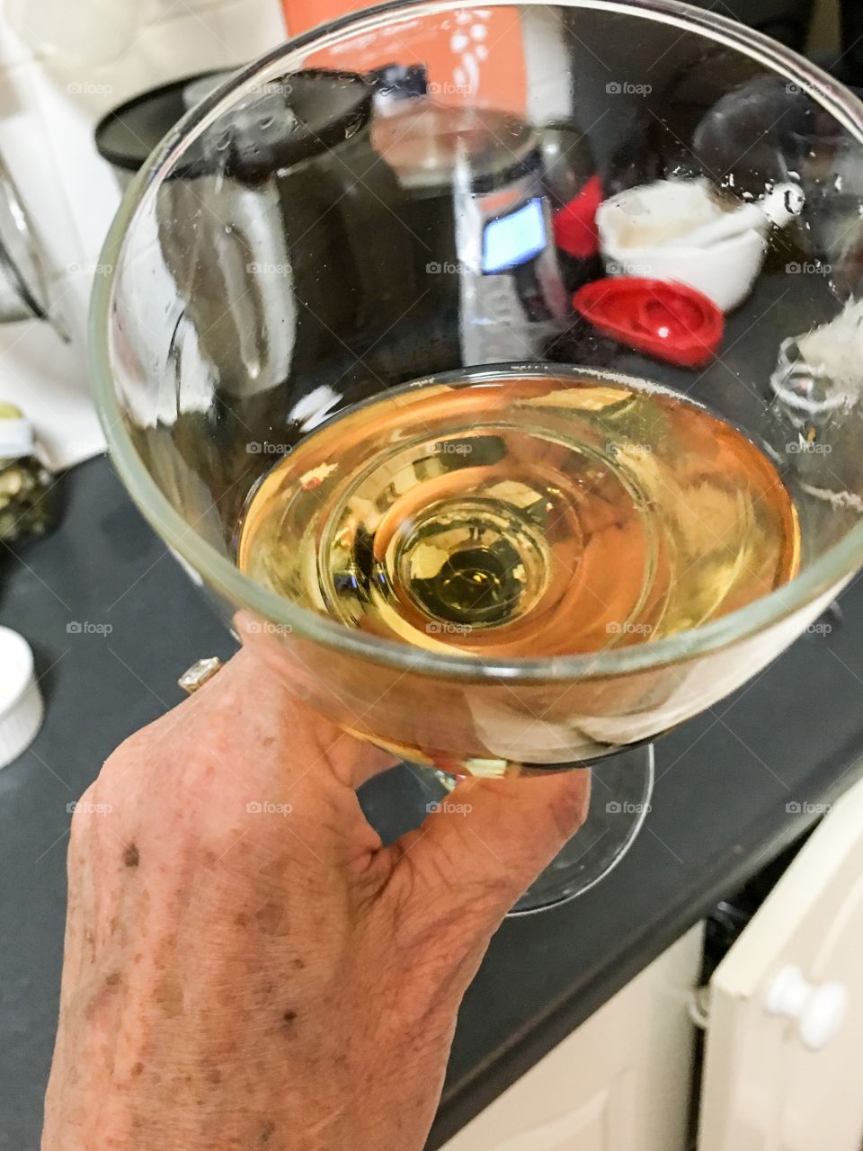 Female hand showing signs of aging ageing aka wrinkles and liver spots holding wine glass in kitchen