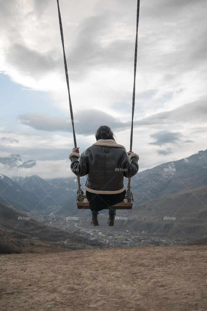 Young girl  swinging on a homemade swing Against the backdrop of cloudy sky and mountain hills.