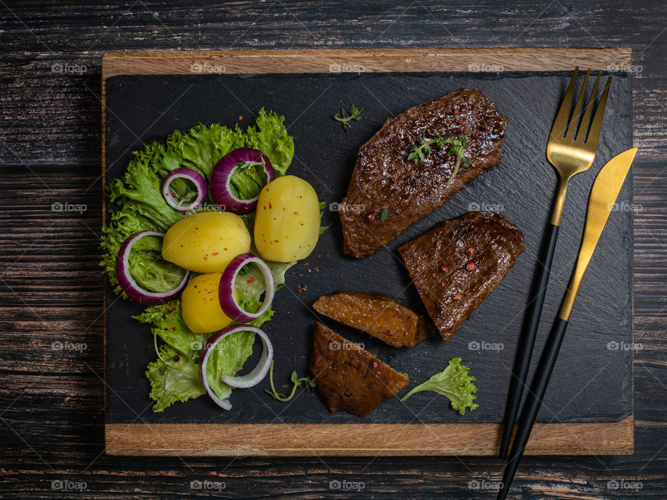 Vegan steak kn a black plate served with potatoes and fresh salad 