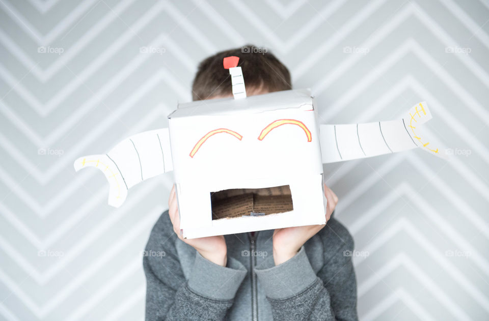 Young boy holding a handmade upcycled cardboard robot in front of his face