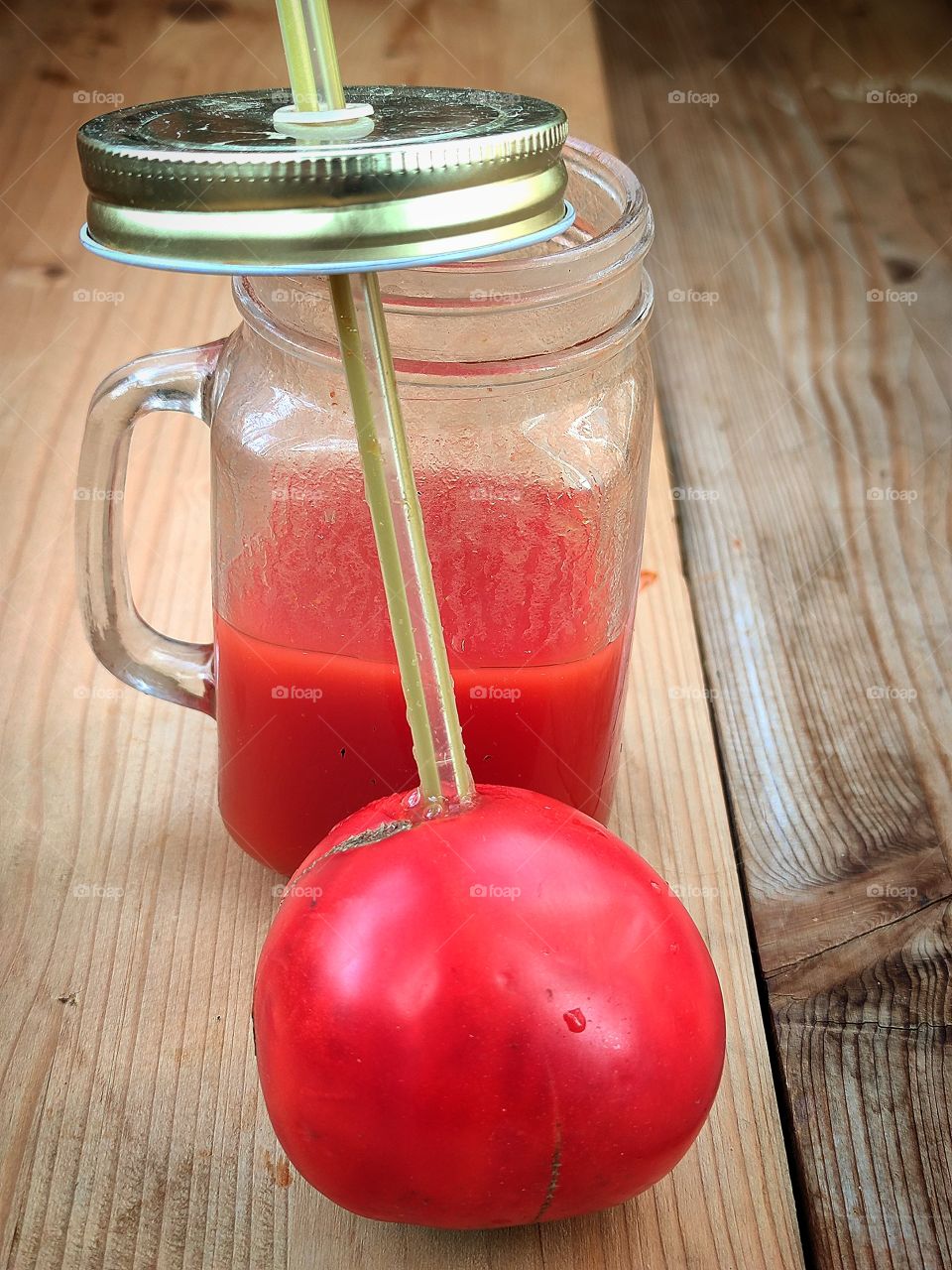 Composition.  Tomato with a straw and a cup of tomato juice