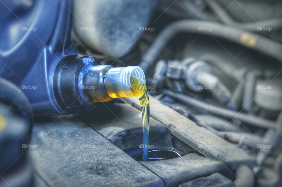 In the photo, the oil in the engine is being changed. beautiful yellow oil pours from a plastic canister under the valve cover of a car