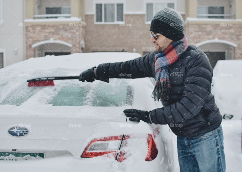 Young man cleaning car in snow 