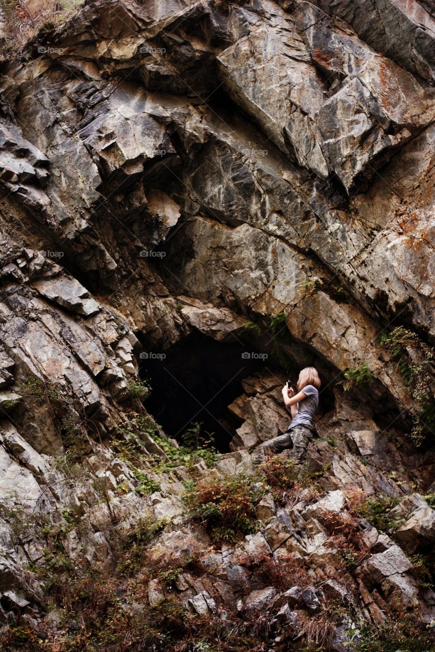 In the campaign, a girl photographs a cave in a rock in the mountains.