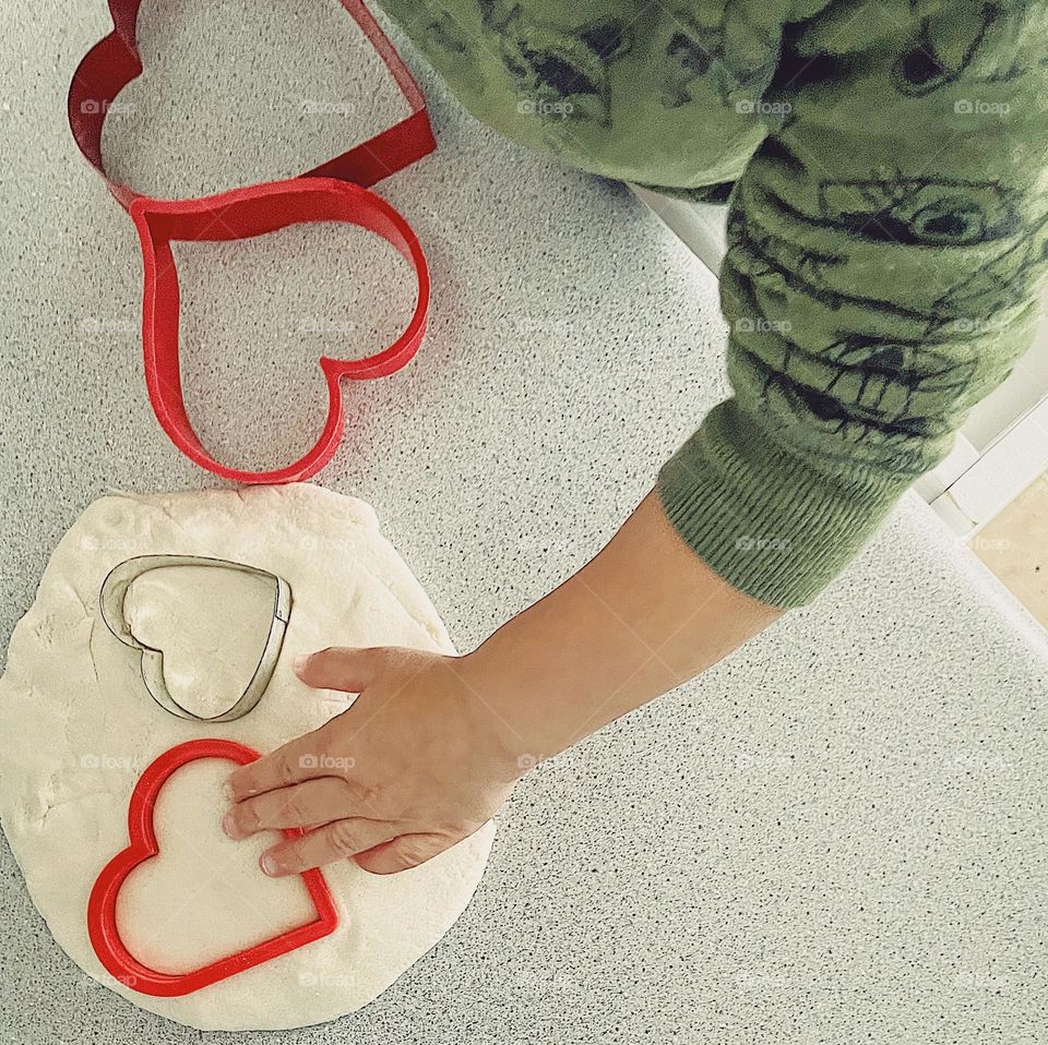 Toddler making heart ornaments for Valentines Day, toddler in the kitchen, toddler helping Mommy, toddler cutting hearts with cookie cutter, toddler making salt dough hearts, making hearts for Valentine’s Day gifts 