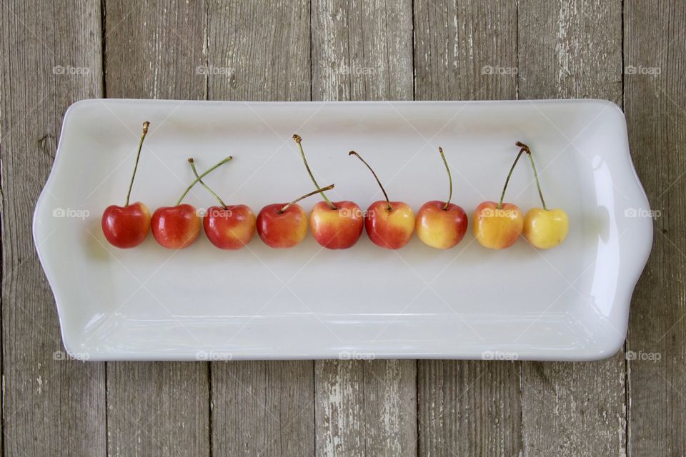 Fruits! - Rainier cherries arranged horizontally by color gradation on a white rectangular plate on a weathered wooden surface in natural light