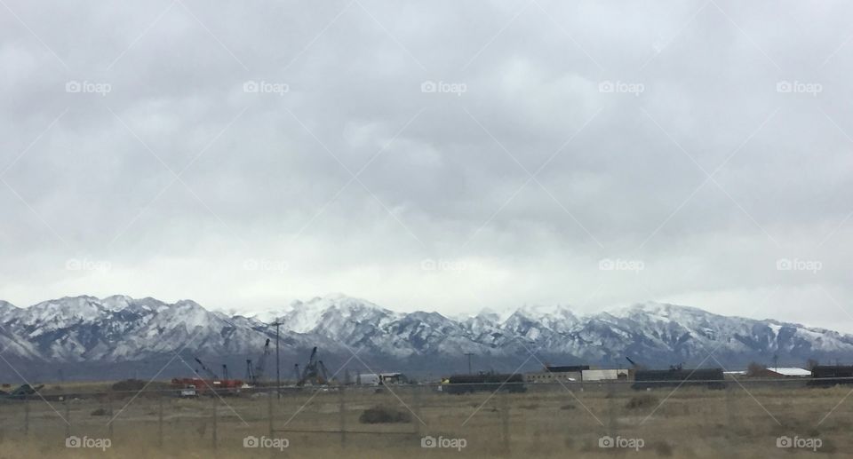 A cloudy winter day in Salt Lake City, Utah. Snow covered mountains sit behind a train track on the side of the road.