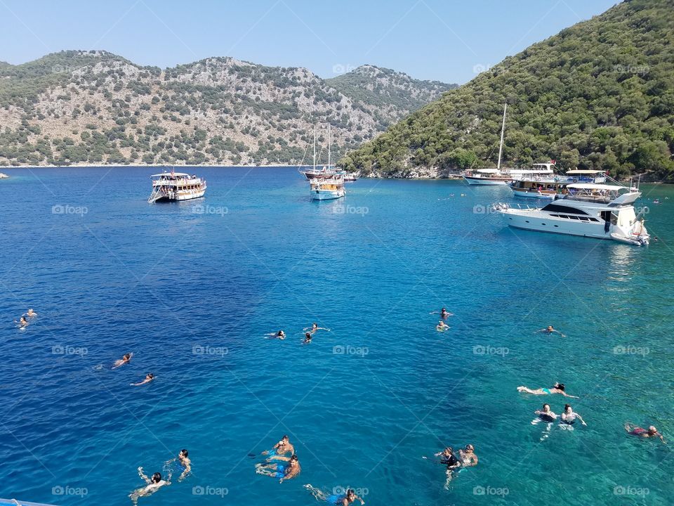 boats in the sea, people swimming, mountains in background, islands