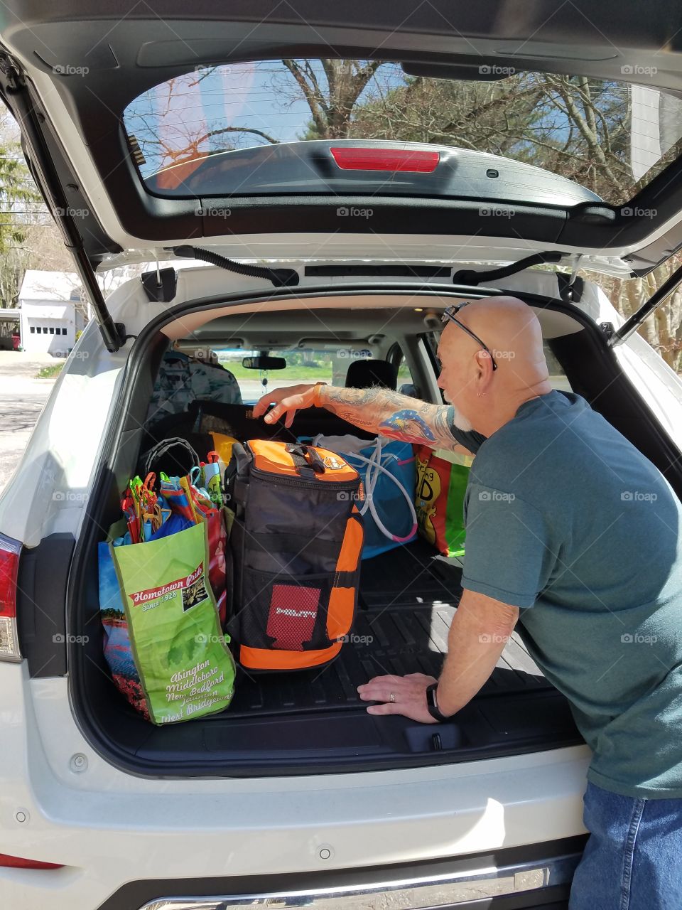 Car with luggage, bags, etc. for road trip. Back lift is open to pack everything needed for the ride. Guy carrying the heavy cooler for easy reaching.