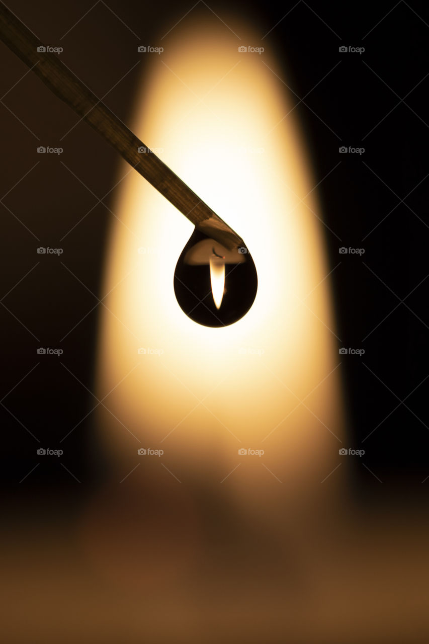 A macro portrait of a silhouette of a drop of water against a flame of a little candle. the candle is refracted in the little droplet.