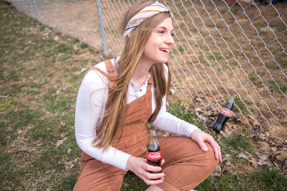 Young millennial woman sitting in the grass and holding a bottle of Coca-cola